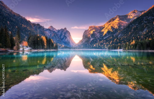 Mountain lake at sunrise in autumn. Landscape with lake, purple sky with gold sunlight, blue fog over the water, reflection, trees with colorful leaves, high rocks in fall. Forest in Dolomites, Italy