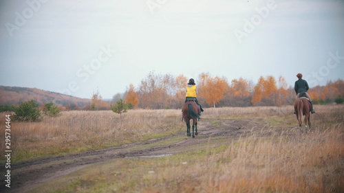 Two women are riding ginger horses on the autumn field