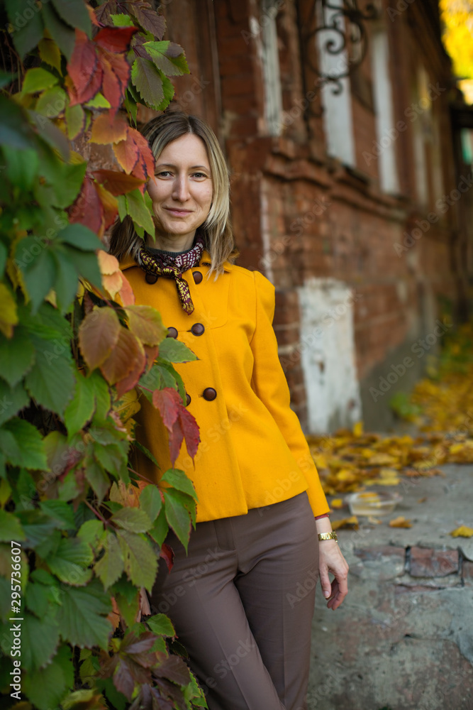 Woman in a yellow jacket poses in an autumn street with red and yellow foliage.