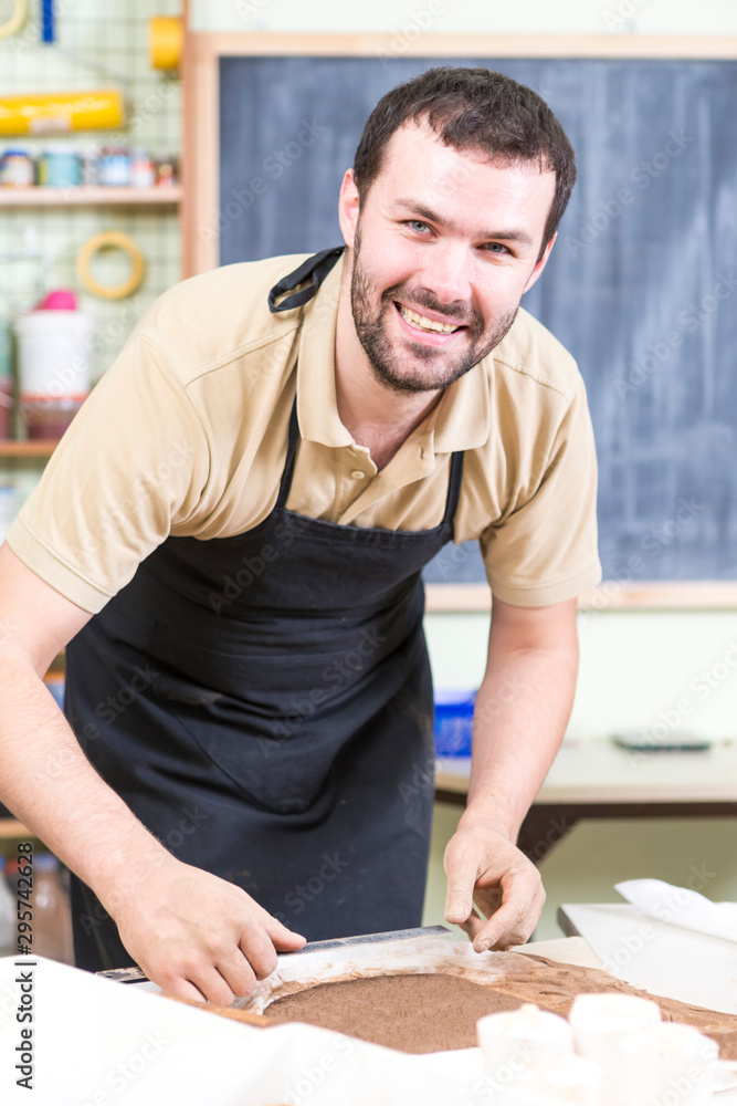 Happy and Smiling Male Potter Preparing a Piece of Wet Clay Using Ruler on The Table in Workshop. Happy and Smiling Male Potter Preparing a Piece of Wet Clay Using Ruler on The Table in Workshop.