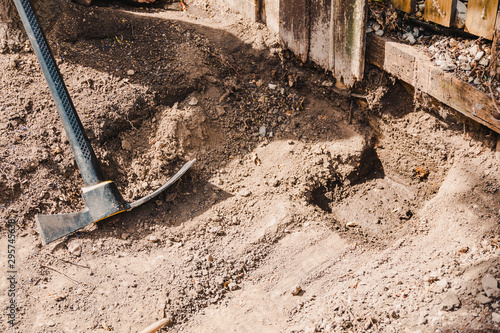 mattock gardening tool to dig the ground and chop weeds left next to fence and hole in the gorund