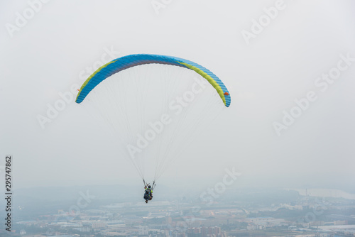 A blue paraglider flying over the plains of the town in gray weather