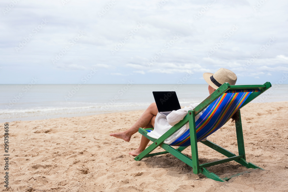 A woman using and typing on laptop computer while lying down on a beach chair