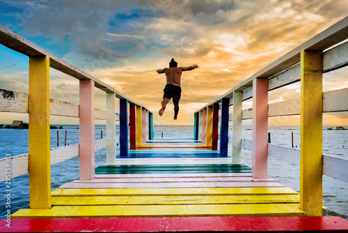 Quadro su tela The young man is jumping into the water on the happy rainbow bridge