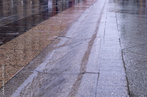 urban street gutter with water flow on tiled sidewalk at rainy day. background, weather.