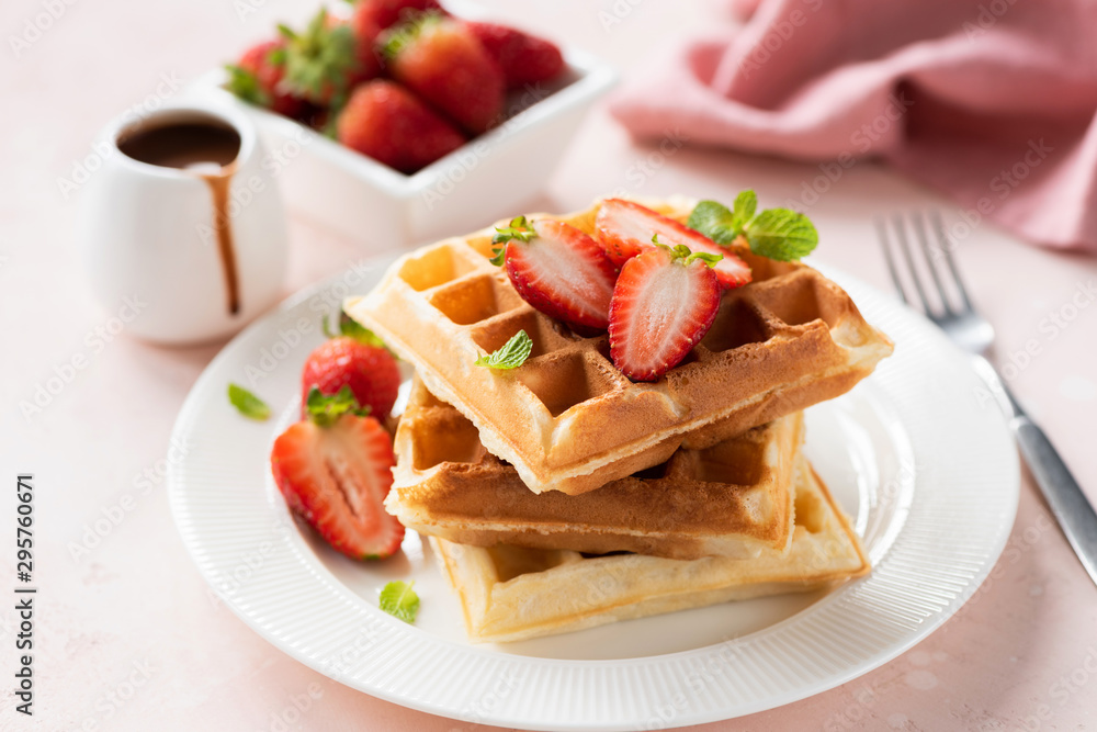 Tasty belgian waffles with strawberries on white plate served with chocolate sauce. Sweet breakfast. Pink background, selective focus