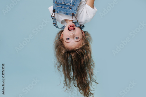 beautiful little girl hanging upside down on blue background