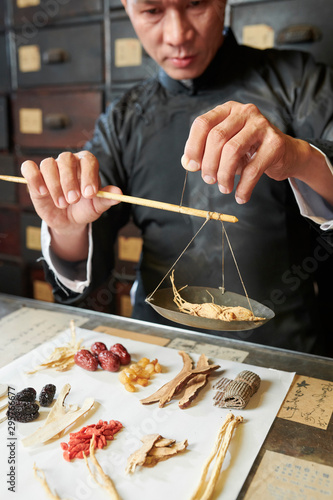 Fotografie Serious traditional Asian medicine practitioner weighting dry ginseng roots on s