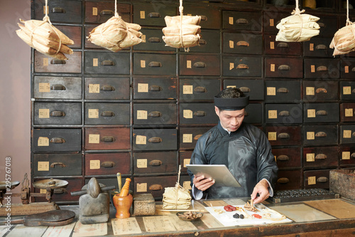 Obraz na plátně Serious traditional Chinese medicine practitioner with tablet computer selecting