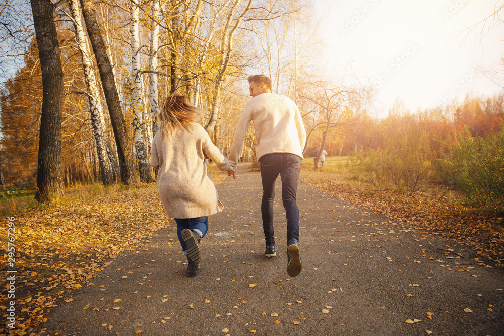 Fototapeta premium Happy couple in love runs through autumn forest, man smile throws maple yellow leaves
