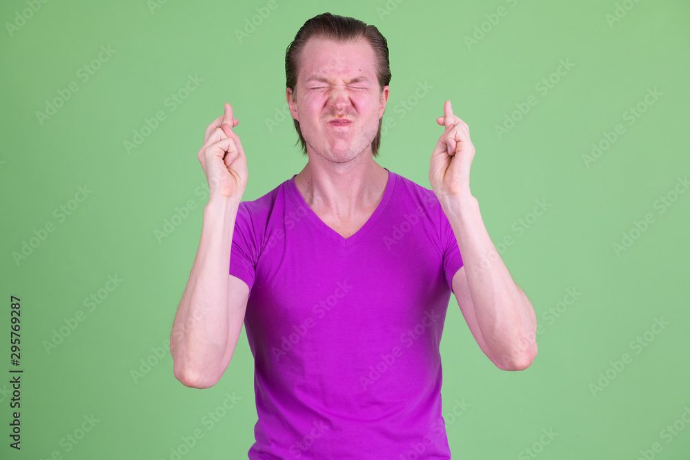 Fototapeta premium Portrait of young handsome man wishing with fingers crossed