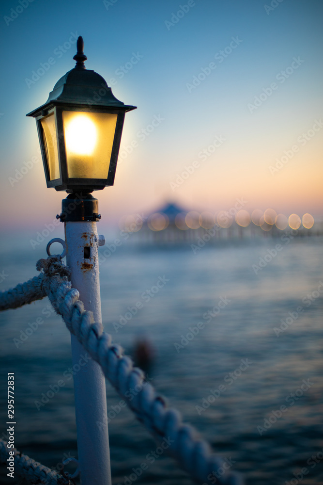 a lantern on a bathing jetty glows bright yellow at dusk
