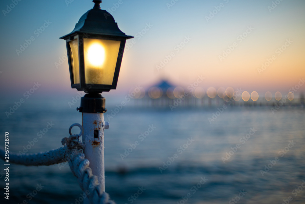 a lantern on a bathing jetty glows bright yellow at dusk