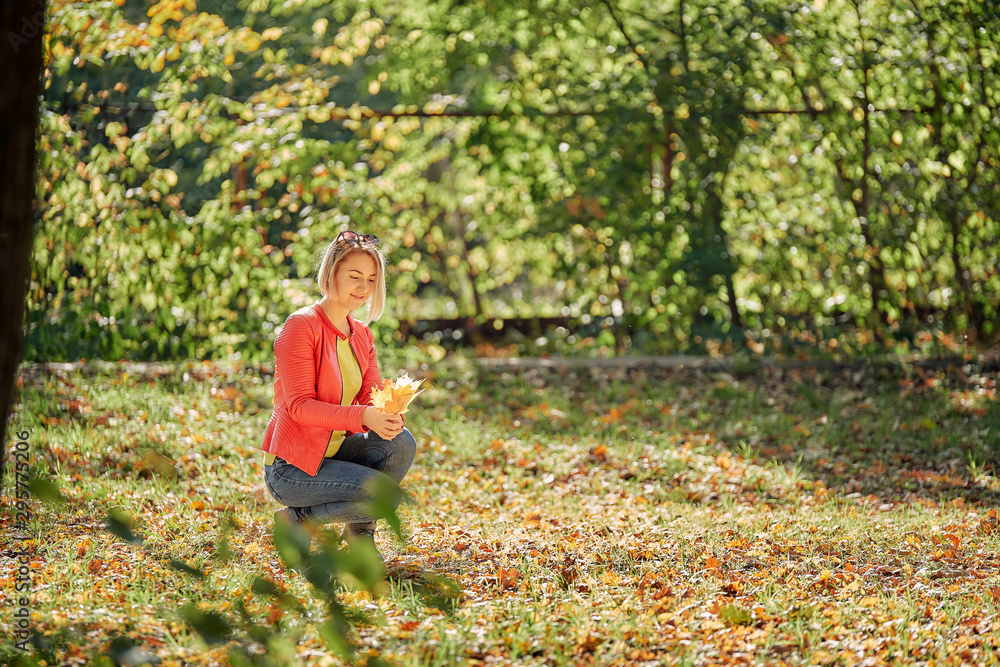 young woman collects fallen leaves in the autumn city park young woman collects fallen leaves in the autumn city park