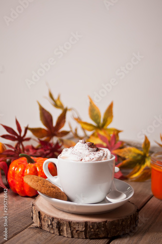 Cup of hot creamy cocoa with froth with autumn leaves and pumpkins on the background