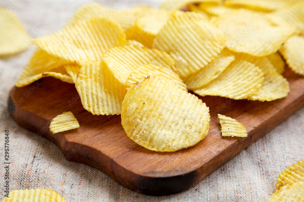 Salted wavy potato chips on a rustic wooden board, side view. Close-up. Salted wavy potato chips on a rustic wooden board, side view. Close-up.