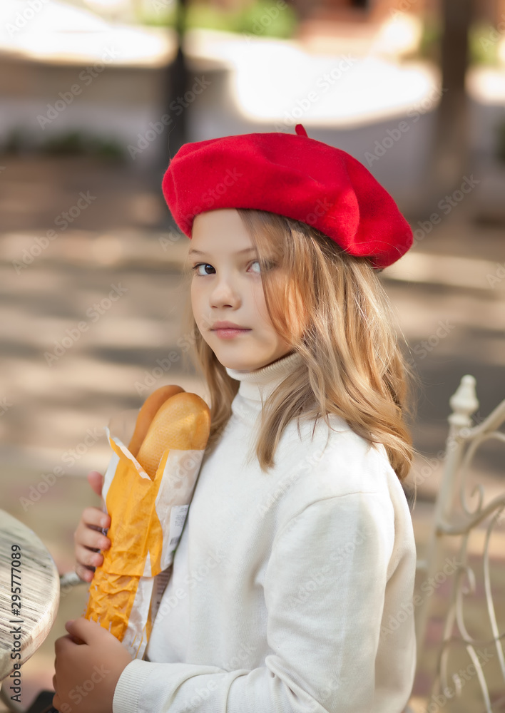 Pretty little girl in a red cap sitting in outdoor cafe with baguette and  smiling. French style Stock-Foto | Adobe Stock