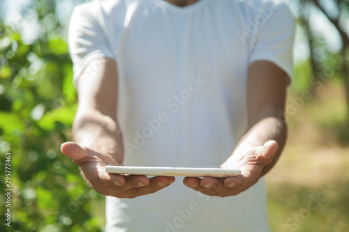 Man holding white digital tablet in nature.