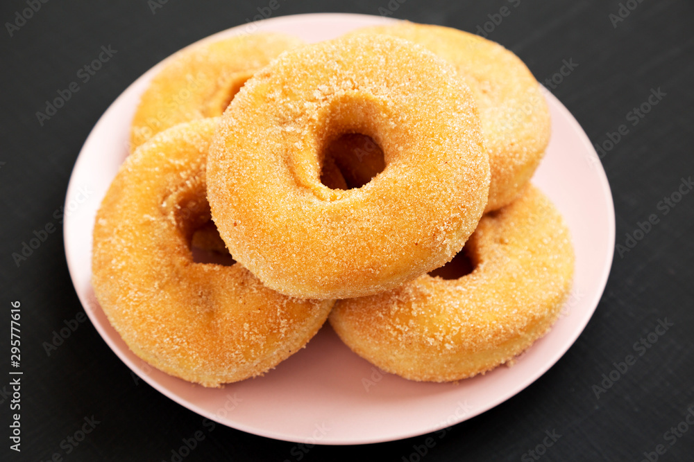 Homemade autumn apple-cinnamon donuts on a pink plate on a black background, low angle view. Close-up.