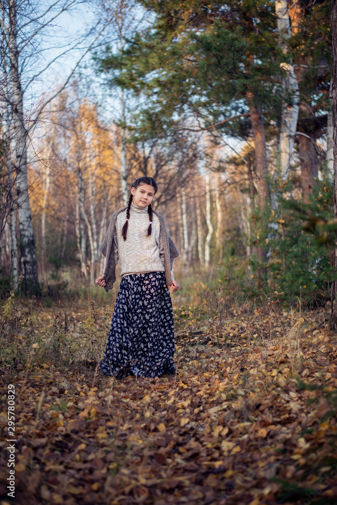 A pretty girl in a long skirt and sweater stands in the autumn forest.
