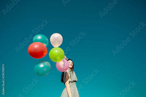 Happy asian woman playing colorful balloons on blue sky background. Freedom concept