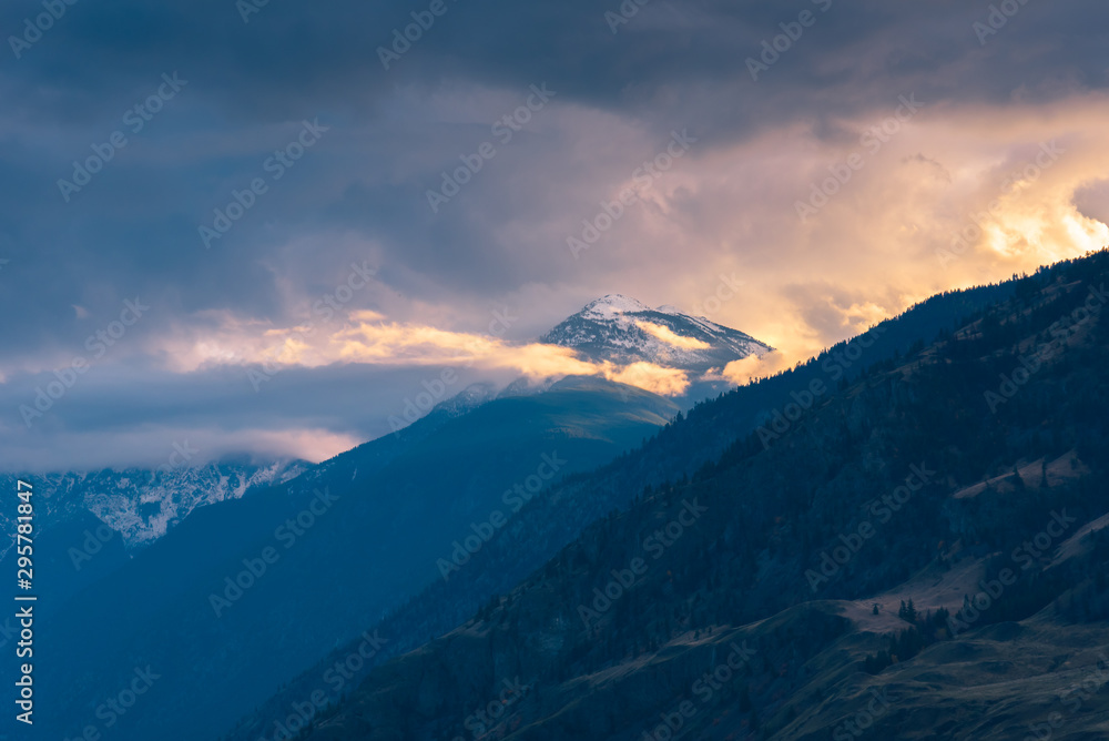 Obraz premium Snow-capped mountain glowing in sunset light with dramatic clouds and fog in Cawston, British Columbia, Canada