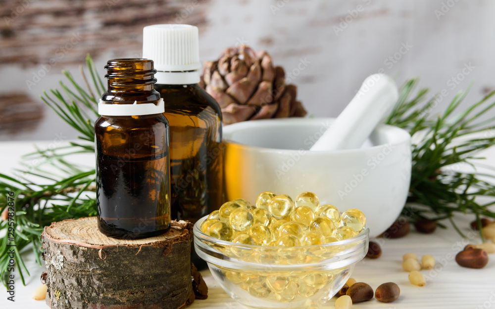 composition of cedar oil with pine nuts on a background of a branch with a pine cone, on a light wooden background composition of cedar oil with pine nuts on a background of a branch with a pine cone, on a light wooden background