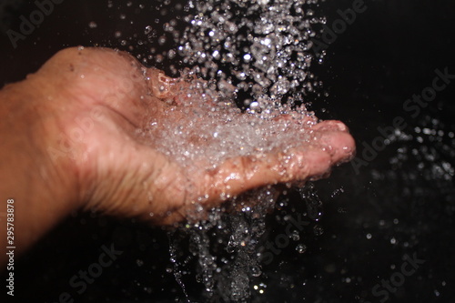 water falling on the man hand on the black background. man enjoying the water falling with his hand.