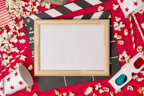 White frame over the clapperboard with popcorns; drinking straws and 3d glasses on red backdrop