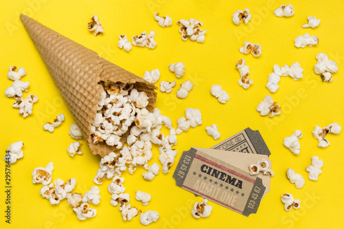 Popcorns spilling from the waffle cone with cinema tickets against yellow backdrop