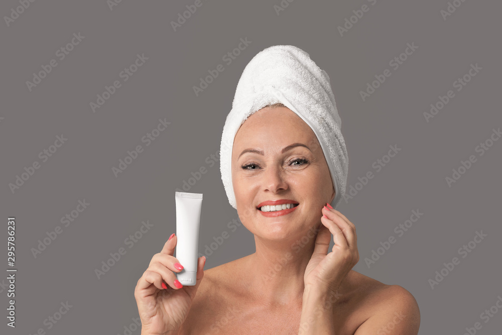 Portrait of beautiful mature woman with perfect skin holding tube of cream  on grey background Stock Photo | Adobe Stock