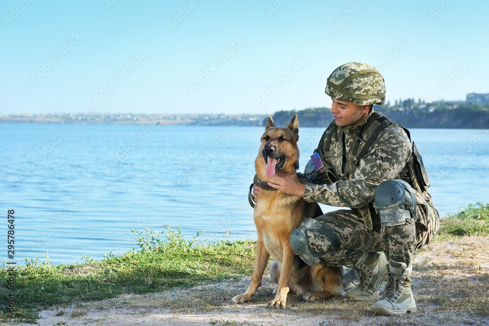 Naklejka premium Man in military uniform with German shepherd dog near river, space for text