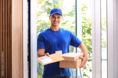 Young courier holding parcels on doorstep. Delivery service photo