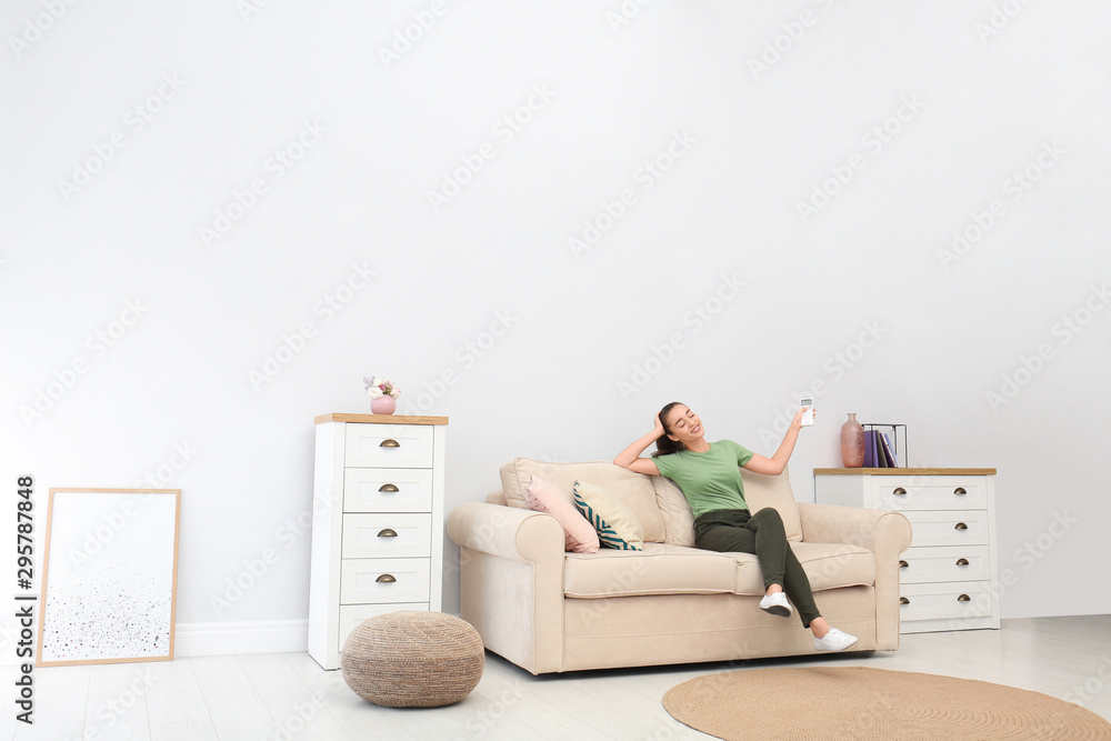Ταπετσαρία Happy young woman switching on air conditioner with remote control at home