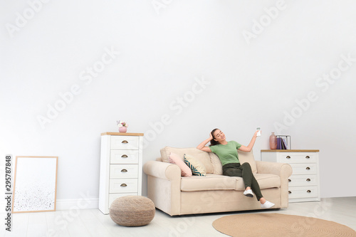 Photography Happy young woman switching on air conditioner with remote control at home