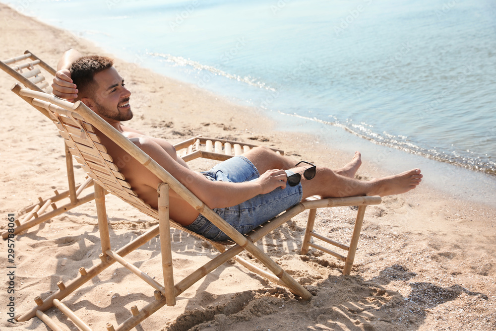 Fototapeta premium Young man relaxing in deck chair on sandy beach