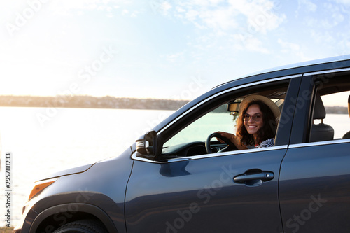 Young beautiful woman sitting in family car on riverside