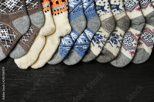 Different knitted socks on black wooden background, flat lay