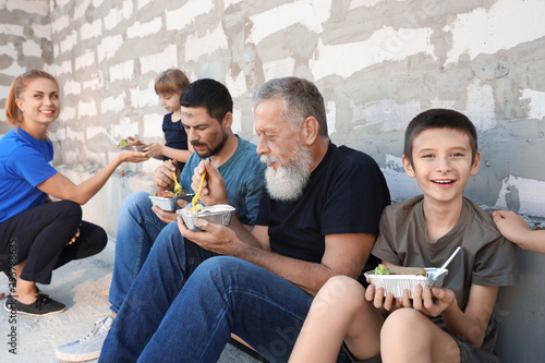 Poor people receiving food from volunteers near wall outdoors