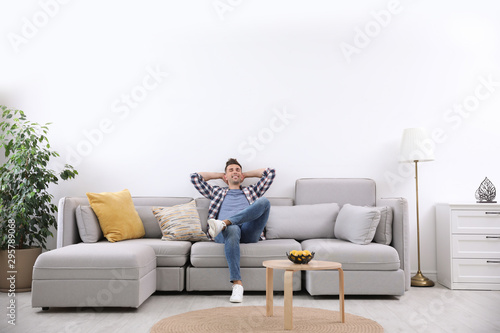 Young man relaxing on sofa under air conditioner at home