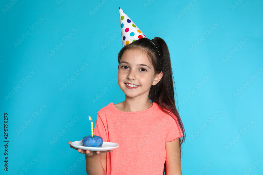 Happy girl holding birthday sweetness with candle on blue background Happy girl holding birthday sweetness with candle on blue background