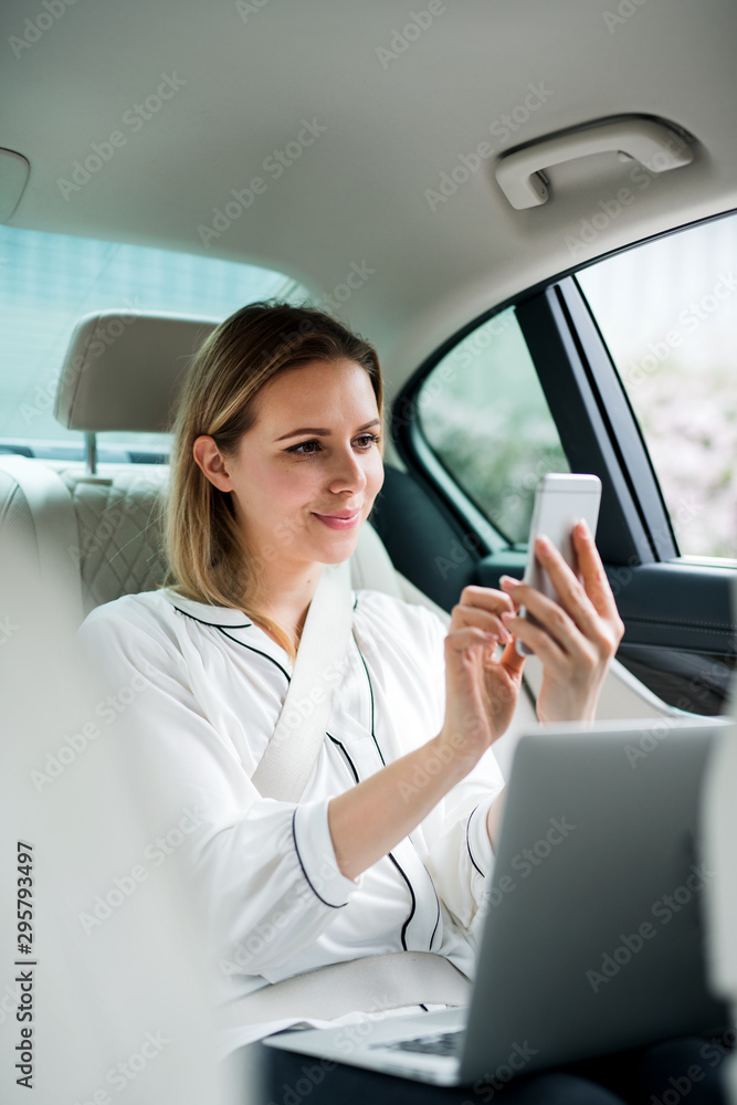 Businesswoman with laptop sitting on back seat in taxi car, taking selfie.