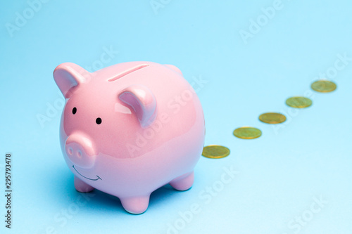 Loss of money. Pink piggy bank losing gold coins on blue background. Bad investment or falling profits