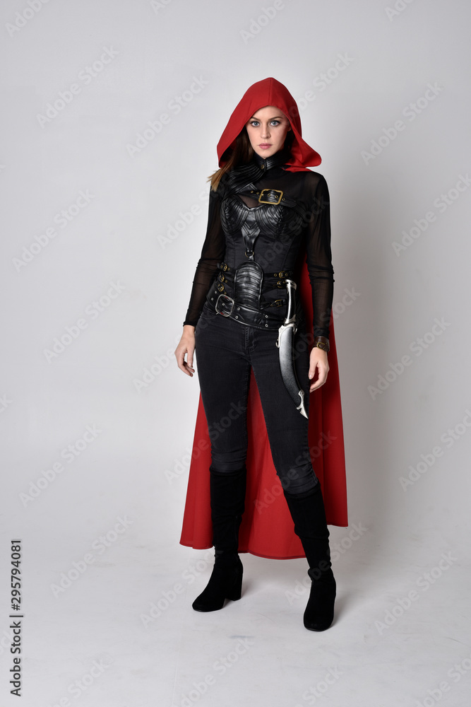 full length portrait of a pretty brunette woman wearing black leather fantasy costume with long red superhero cape. standing pose on a studio background. full length portrait of a pretty brunette woman wearing black leather fantasy costume with long red superhero cape. standing pose on a studio background.