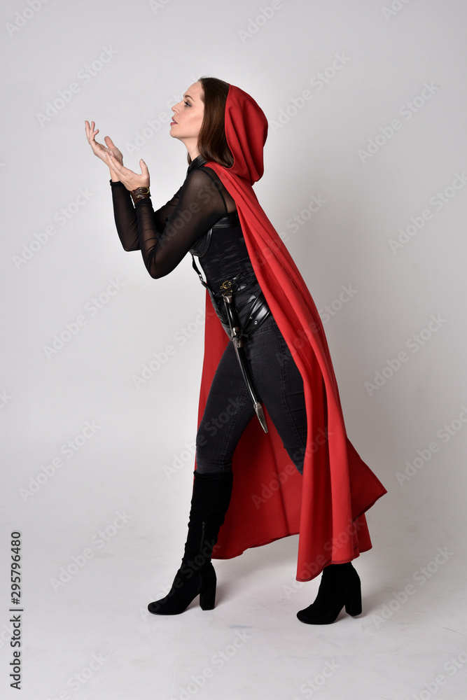 full length portrait of a pretty brunette woman wearing black leather fantasy costume with long red superhero cape. standing pose on a studio background. full length portrait of a pretty brunette woman wearing black leather fantasy costume with long red superhero cape. standing pose on a studio background.