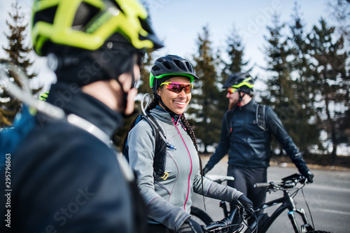 Group of mountain bikers standing on road outdoors in winter, talking.