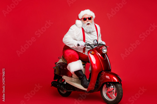 Portrait of his he nice bearded cool cheerful funky Santa hipster riding retro moped December ho-ho-ho North Pole destination isolated on bright vivid shine vibrant red color background