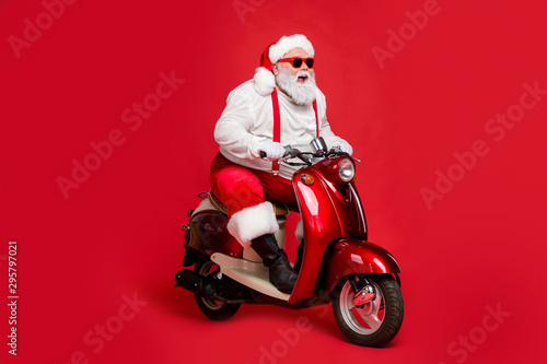Portrait of his he nice bearded cool cheerful cheery funky Santa hipster riding retro moped December sport isolated on bright vivid shine vibrant red color background