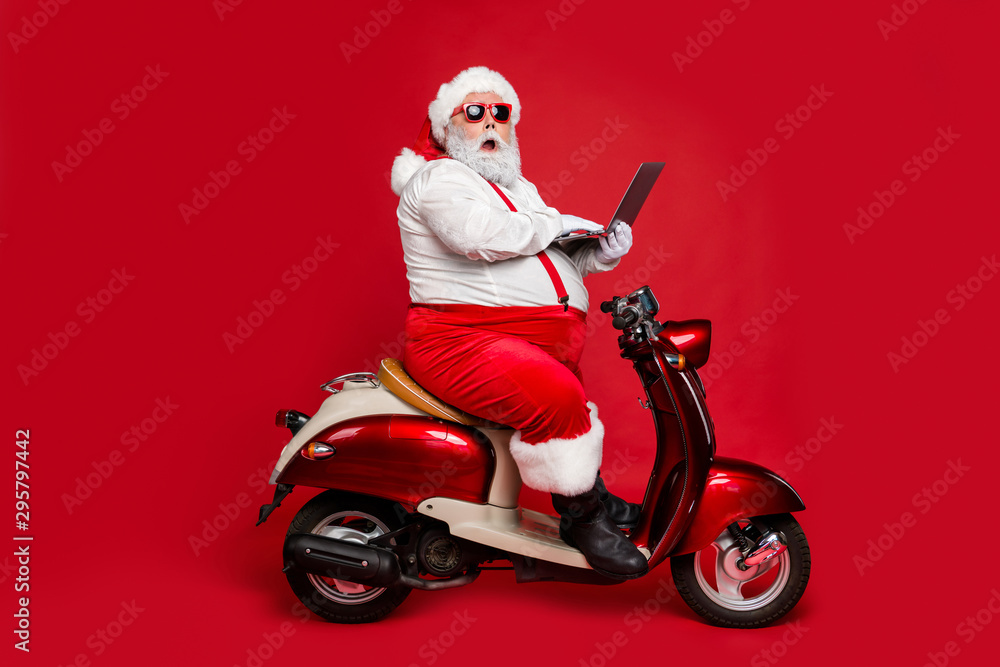 Profile side view of his he nice fat wondered funky Santa sitting on moped holding in hand laptop reading wish dream list winter fairy isolated on bright vivid shine vibrant red color background Profile side view of his he nice fat wondered funky Santa sitting on moped holding in hand laptop reading wish dream list winter fairy isolated on bright vivid shine vibrant red color background