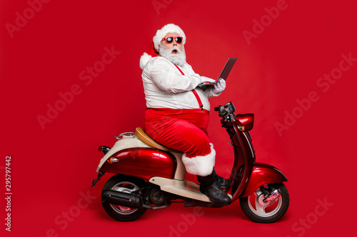 Profile side view of his he nice fat wondered funky Santa sitting on moped holding in hand laptop reading wish dream list winter fairy isolated on bright vivid shine vibrant red color background